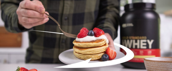 Optimum Nutrition Gold Standard 100% Whey Protein container next to a plate of pancakes with berries