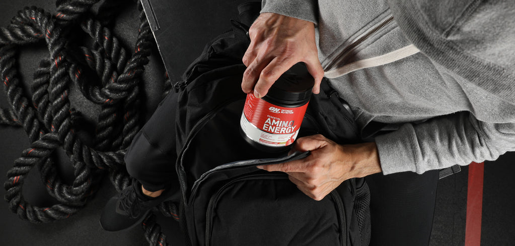 Optimum Nutrition Amino Energy supplement jar being placed into a gym bag, suitable for post-workout nutrition
