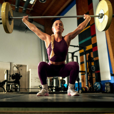 Person performing an overhead squat with a barbell in a gym setting