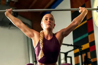 A person lifting a barbell overhead in a gym setting, demonstrating strength training