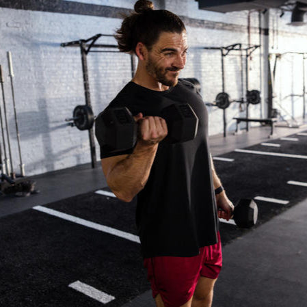 Man lifting dumbbells in a gym setting, performing a bicep curl exercise