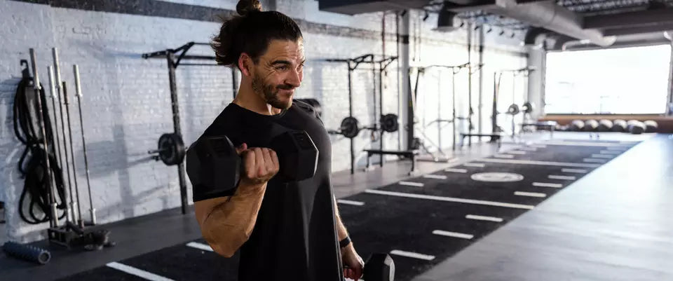 Man lifting dumbbells in a gym setting, performing a bicep curl exercise