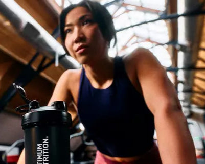 Person exercising indoors with a shaker bottle labeled "Optimum Nutrition."