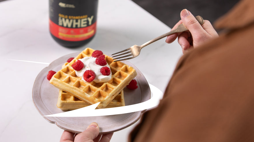 Gold Standard 100% Whey protein powder container next to a plate of waffles topped with whipped cream and raspberries