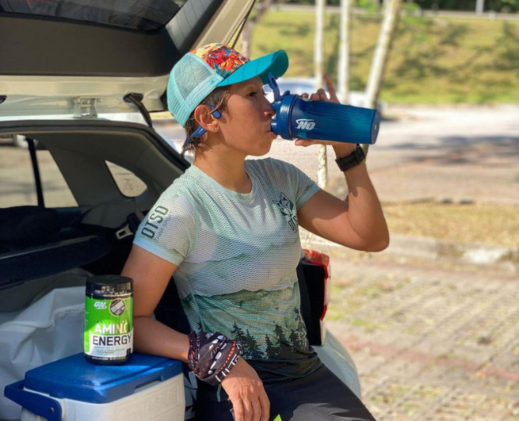 Person drinking from an Optimum Nutrition shaker bottle next to a container of ON Amino Energy