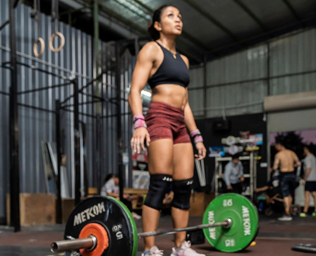 A person standing in a gym near a barbell, possibly preparing for a high-intensity workout