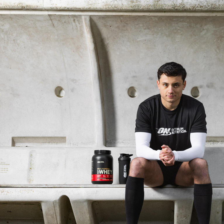 Optimum Nutrition athlete sitting on a bench with Optimum Nutrition Gold Standard Whey protein powder and shaker bottle