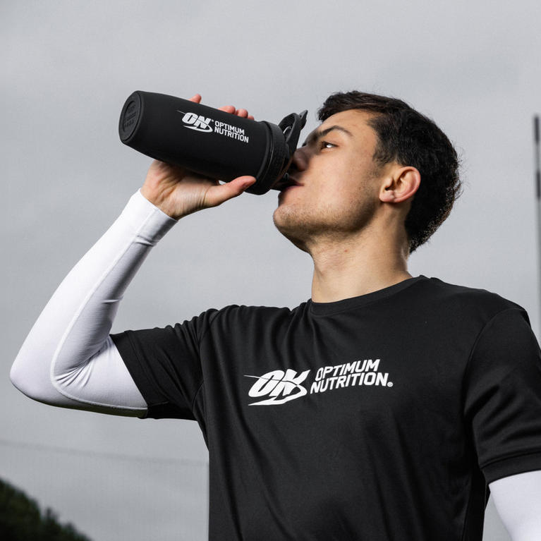 Person drinking from an Optimum Nutrition shaker bottle, wearing an Optimum Nutrition branded shirt