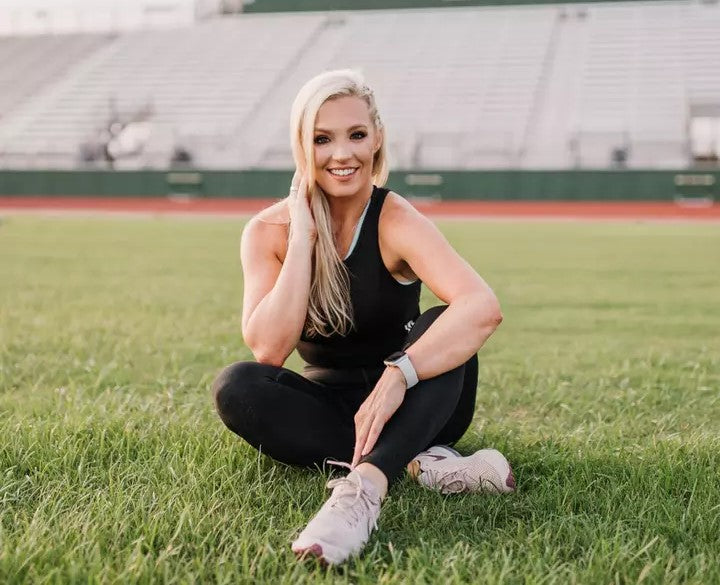 A person sitting on grass in a sports field, wearing athletic clothing and sneakers