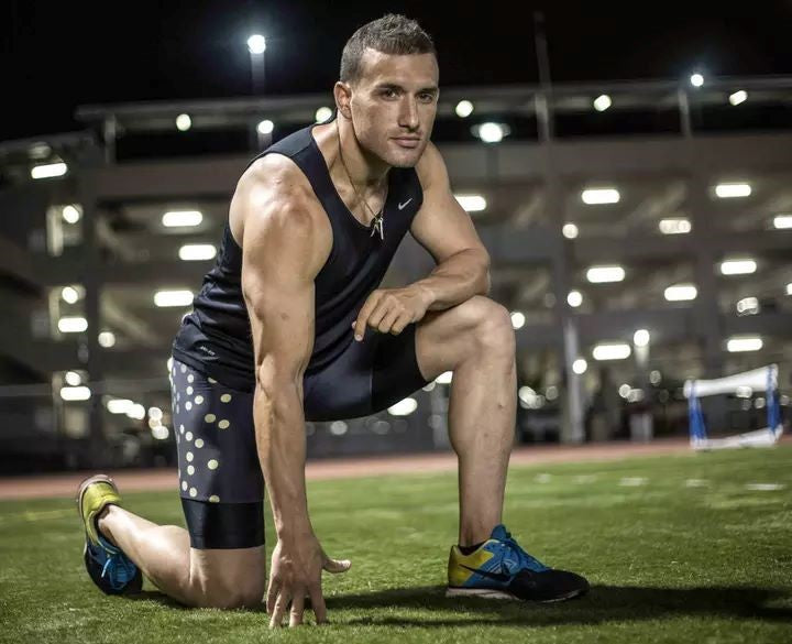 Athlete in athletic gear kneeling on a sports field, preparing for a run or workout