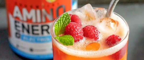 Amino energy drink with ice, raspberries, and mint garnish in a glass, next to an Amino Energy supplement container