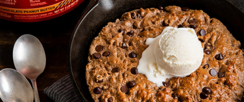 Chocolate chip skillet cookie topped with a scoop of vanilla ice cream, with a container of Optimum Nutrition protein powder in the backgrou