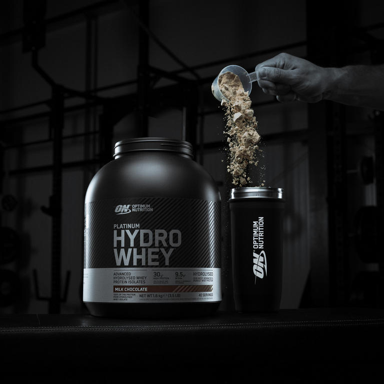 Optimum Nutrition Platinum Hydro Whey protein powder container with a scoop pouring powder into a shaker cup