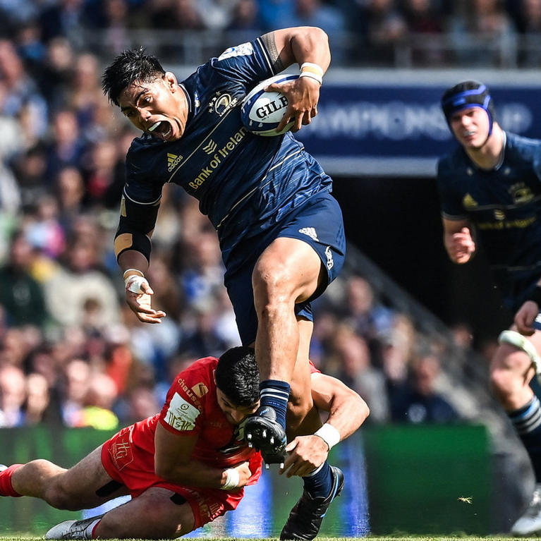 Rugby player in blue jersey running with the ball, evading a tackle from an opponent in red
