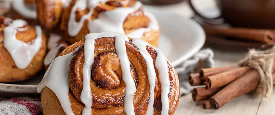 Cinnamon rolls with icing on a plate, accompanied by cinnamon sticks