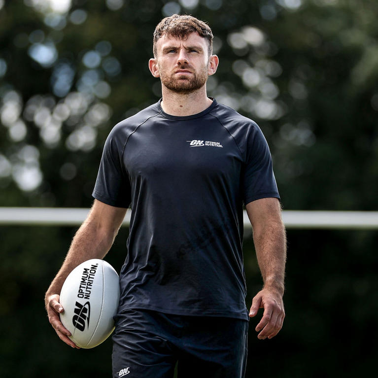 A person holding a rugby ball with the Optimum Nutrition logo, wearing Optimum Nutrition branded athletic clothing