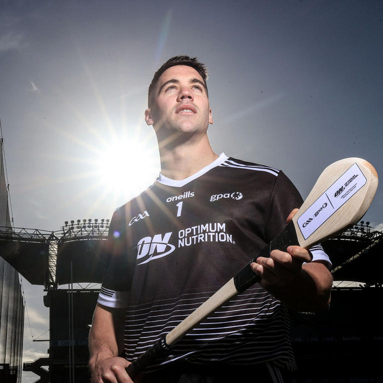 A person holding a hurling stick, wearing a jersey with the Optimum Nutrition logo