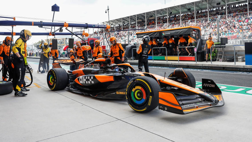 A Formula 1 car in the pit lane during a race, surrounded by a pit crew in orange uniforms
