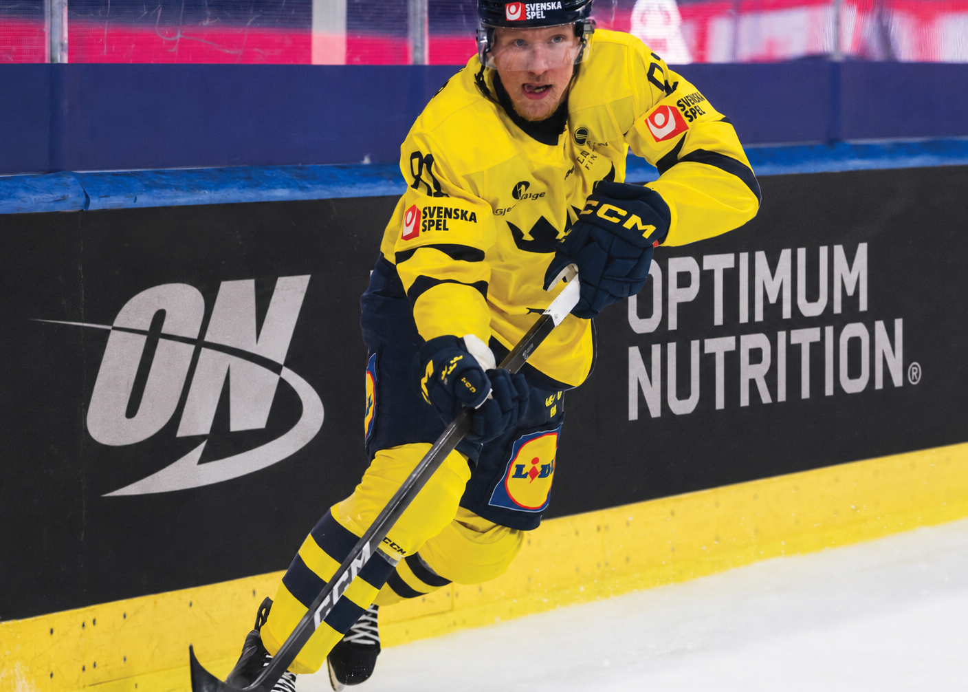 Hockey player in a yellow uniform on an ice rink with advertisements in the background
