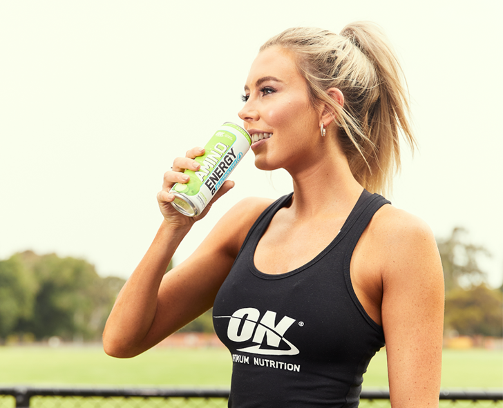 Woman drinking Optimum Nutrition energy drink, wearing ON branded tank top, outdoors