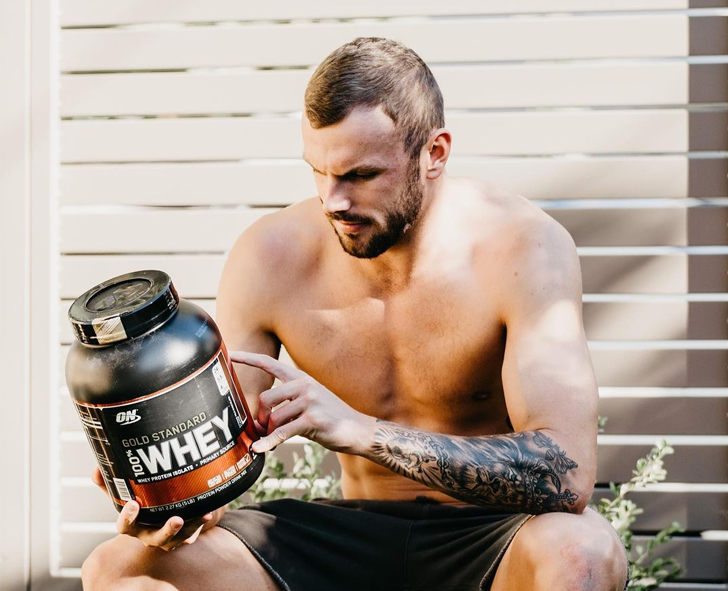 Optimum Nutrition Gold Standard 100% Whey Protein, 2.73 kg container, held by a person