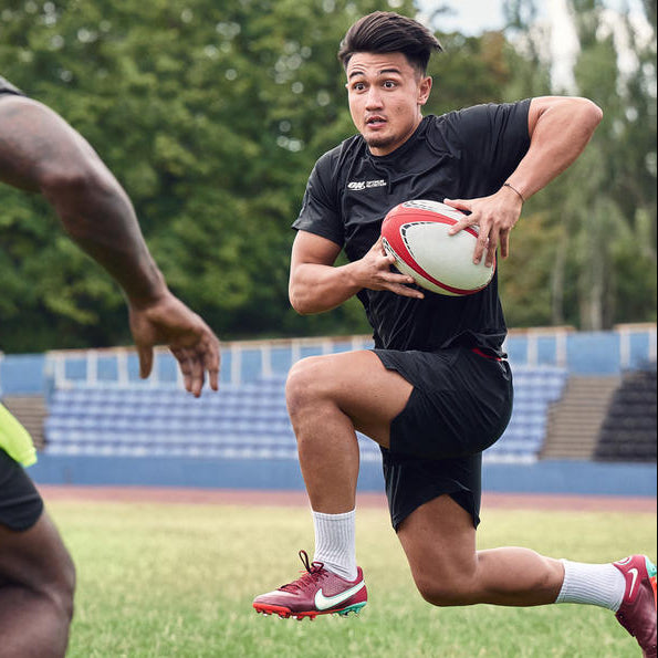 Two athletes playing rugby on a field, one running with the ball while the other prepares to tackle