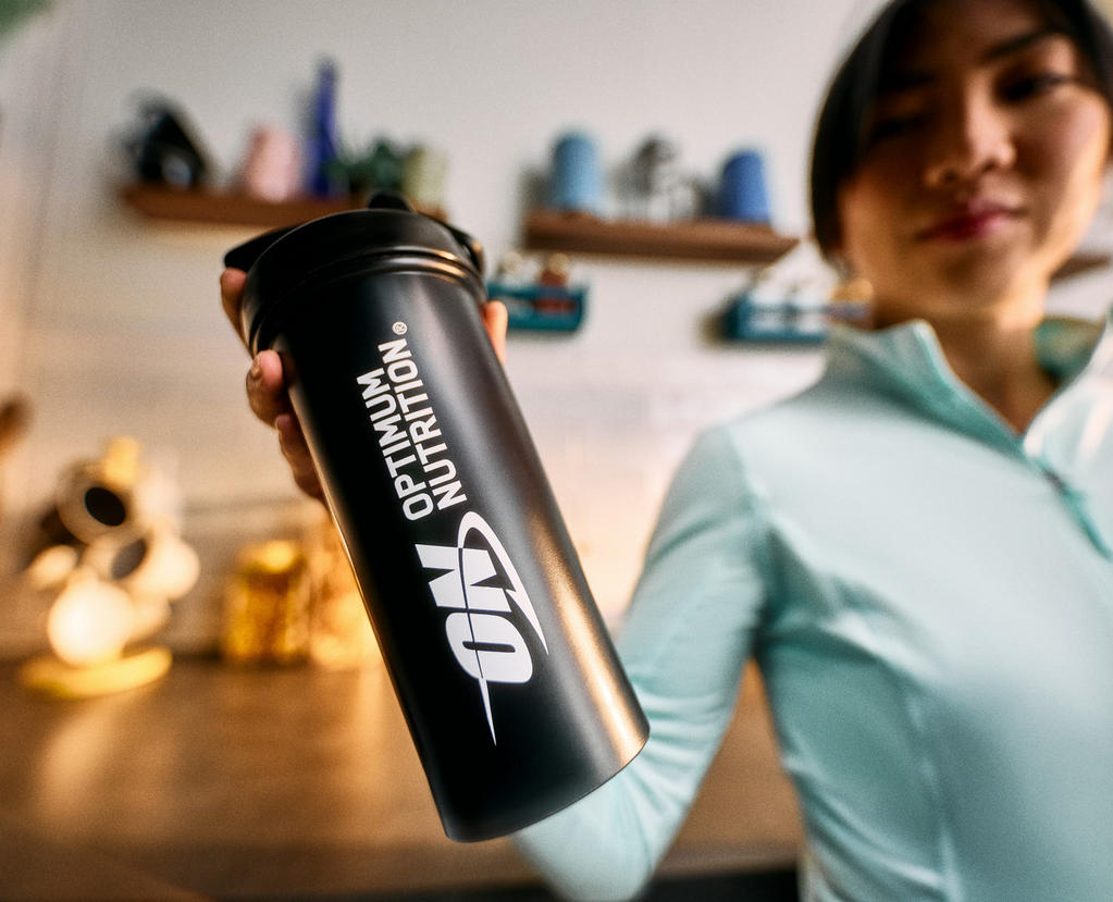 Optimum Nutrition shaker bottle held by a person in workout attire, used for mixing supplements