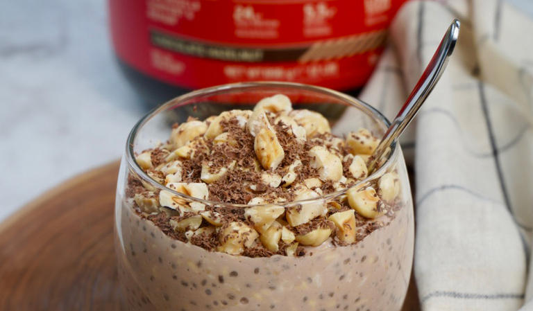 Glass of protein-rich oatmeal topped with chopped nuts and chocolate shavings, with a spoon