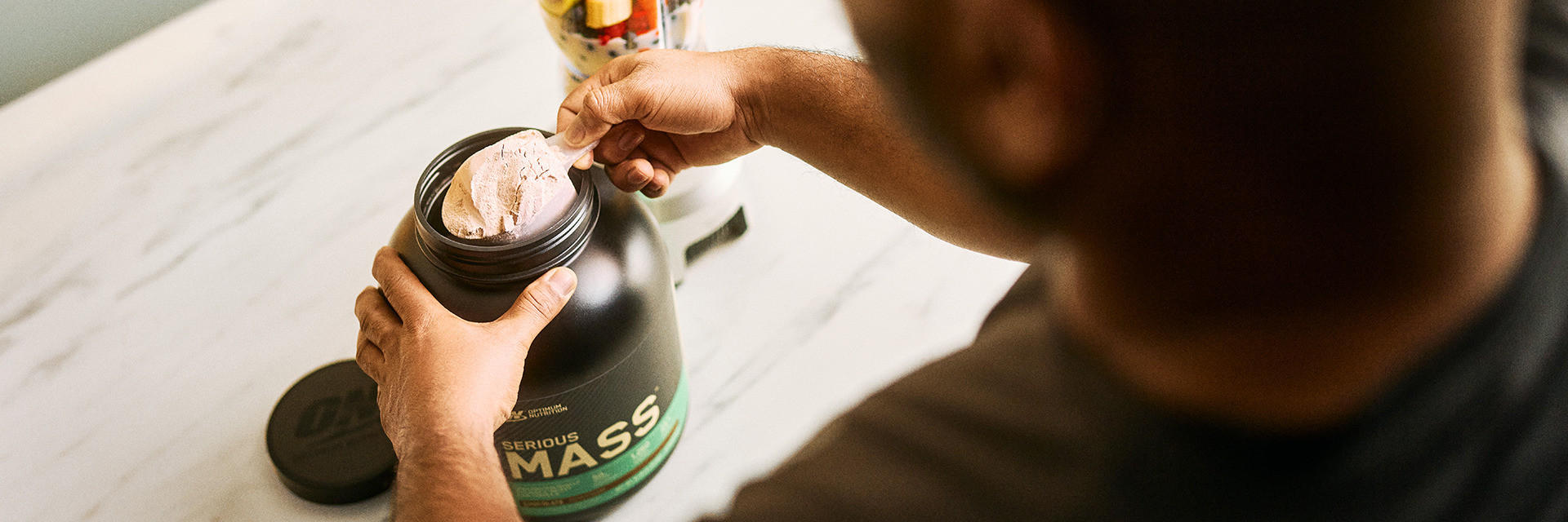 Optimum Nutrition Serious Mass Weight Gainer container being scooped by a person, suitable for post-workout nutrition and muscle building