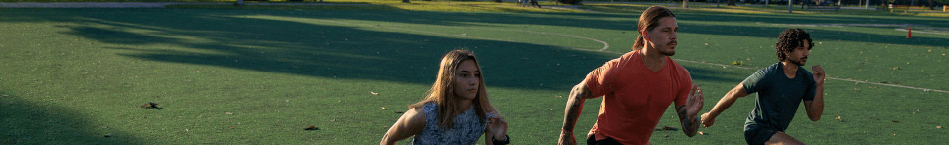 Three people running on a grassy field, engaging in outdoor exercise