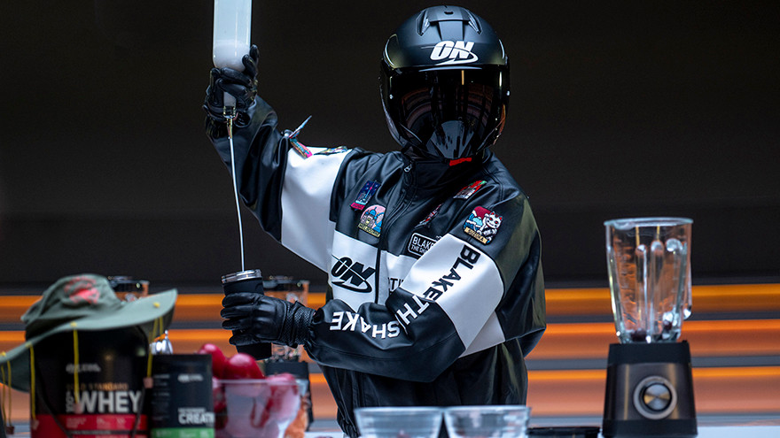Person in a racing suit and helmet preparing a protein shake with ON supplements and a blender