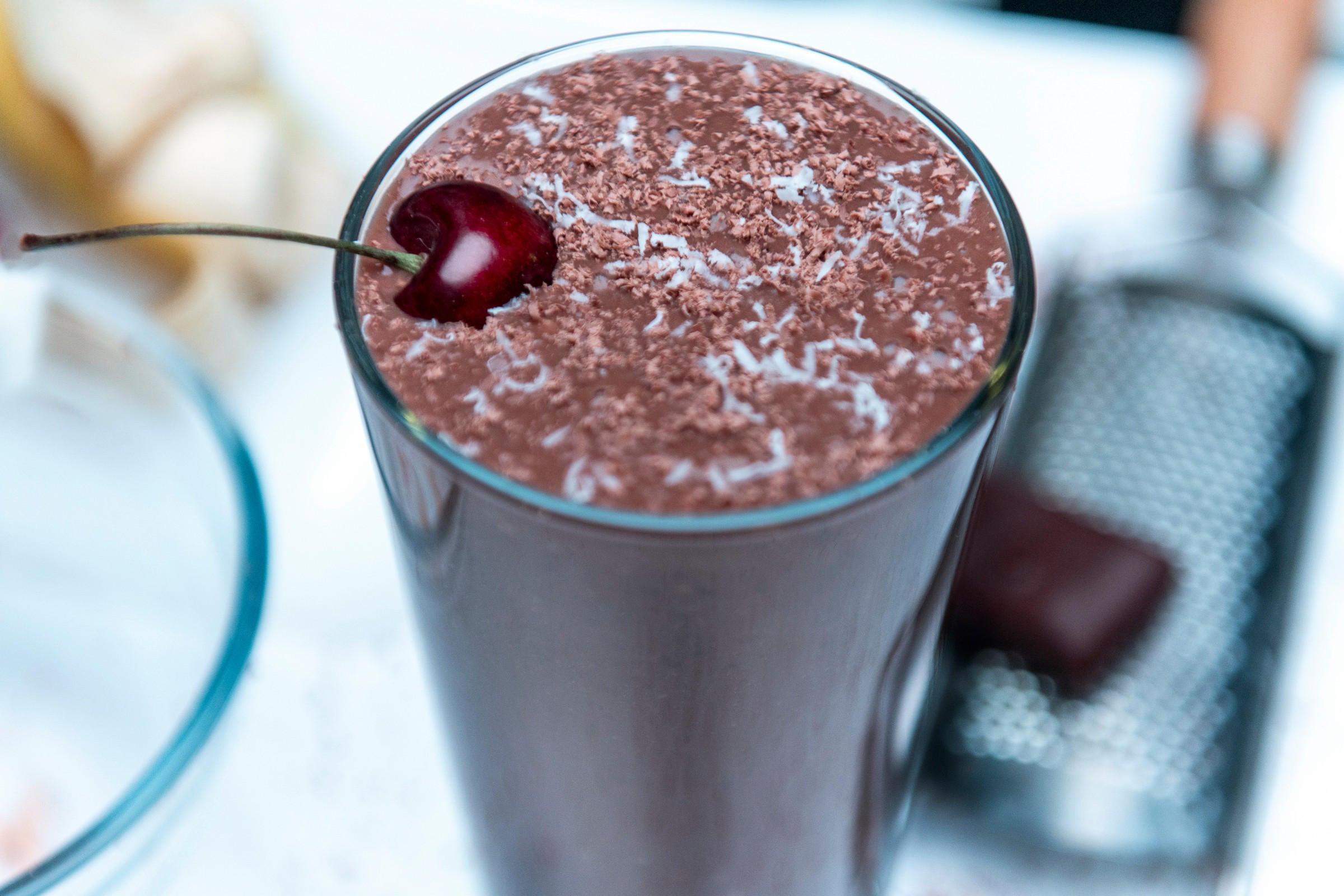 Chocolate protein shake topped with grated chocolate and a cherry, suitable for post-workout nutrition and muscle building