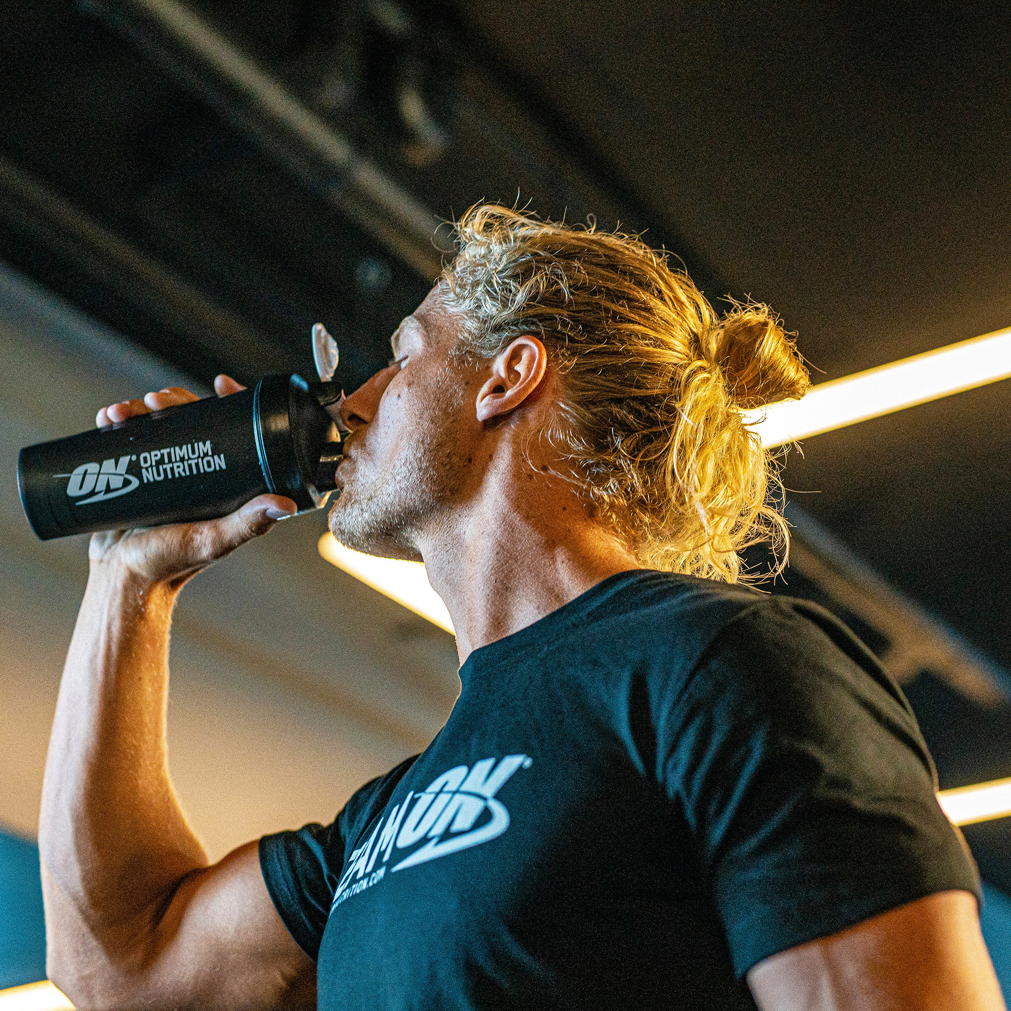 A person drinking from an Optimum Nutrition shaker bottle, likely using it for protein or amino energy supplementation