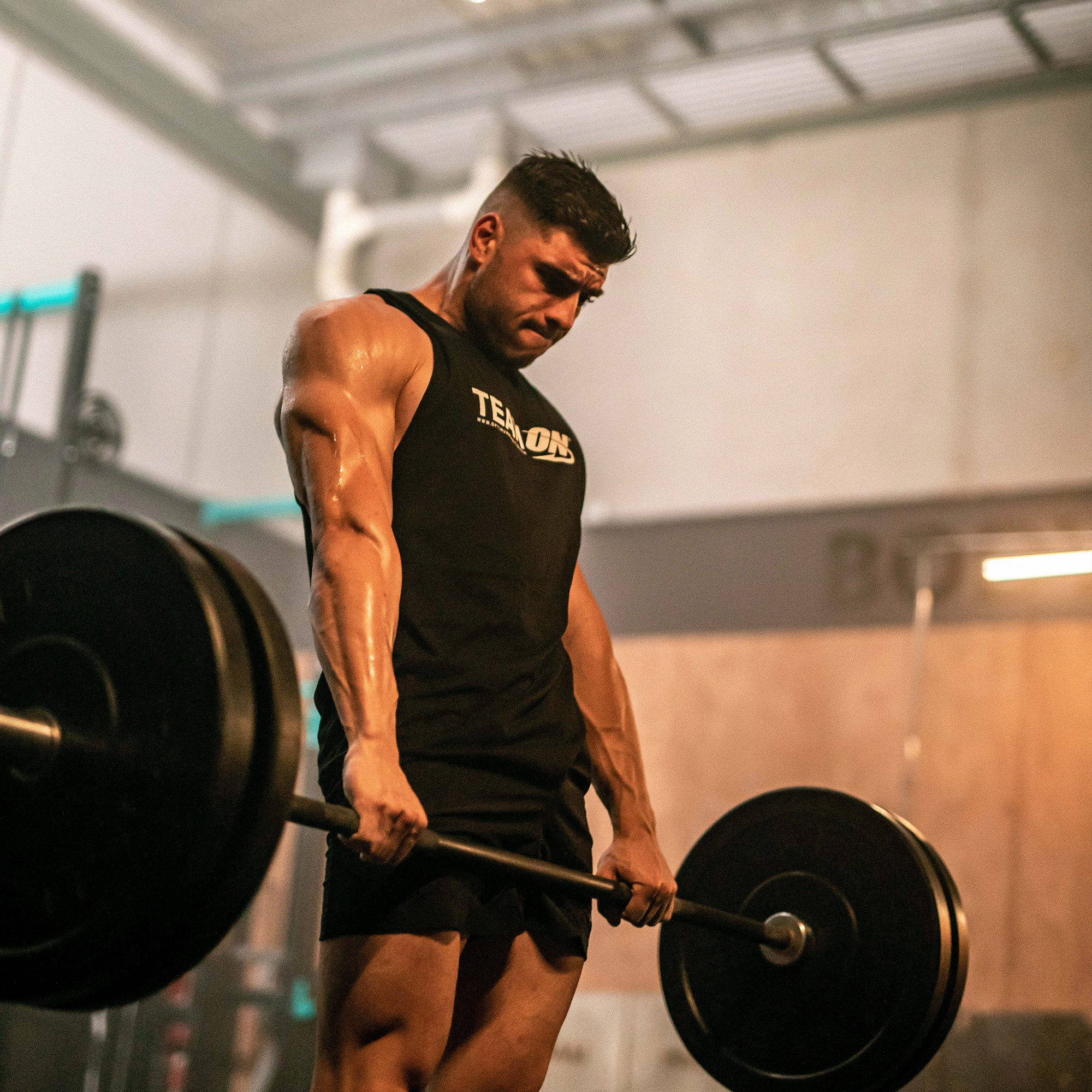 Man lifting a barbell in a gym setting, wearing a sleeveless shirt with "Team ON" visible