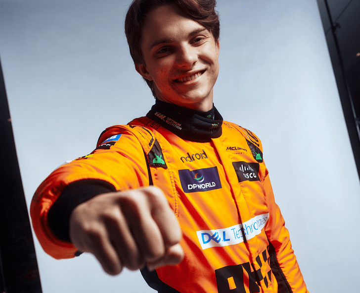 Oscar piastri wearing an orange racing suit with visible branding, pointing forward