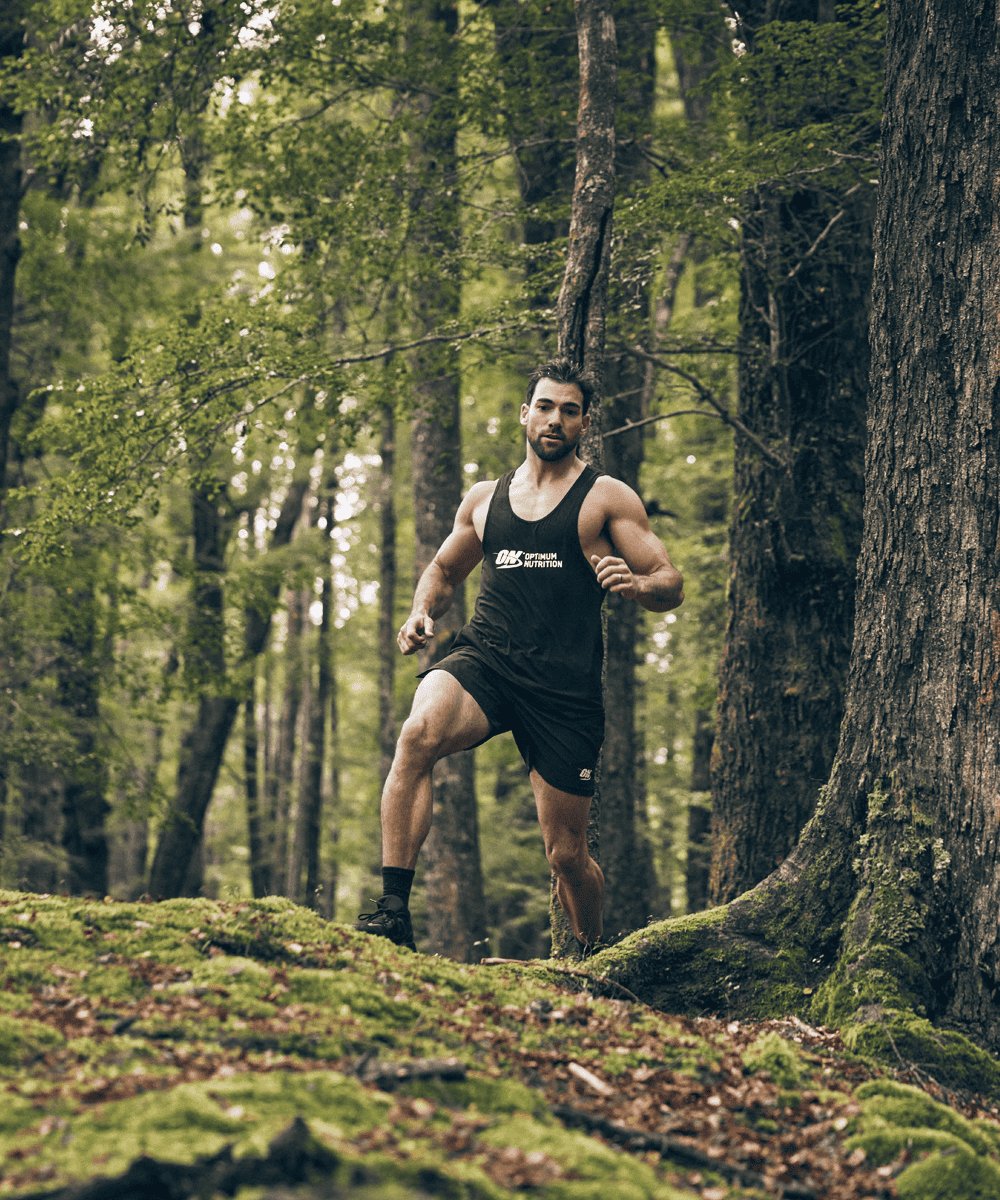Man jogging in a forest wearing a tank top with "ON" logo, promoting fitness and active lifestyle