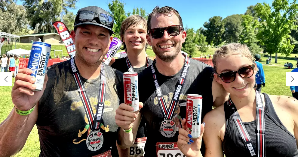 Group of people holding cans of Amino Energy drinks, wearing medals, likely after a fitness event