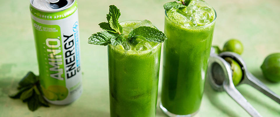 Amino Energy drink, green apple flavor, with two glasses of green smoothie garnished with mint leaves