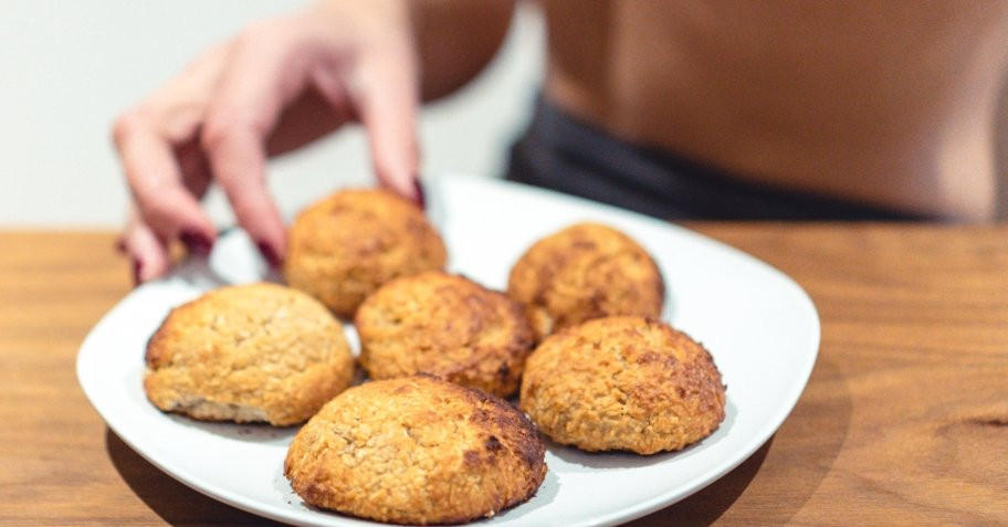 Plate of baked cookies on a wooden table, with a person's hand reaching for one