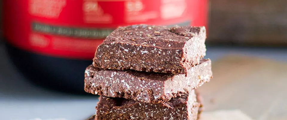 Protein bars stacked on a table with a container of whey protein powder in the background