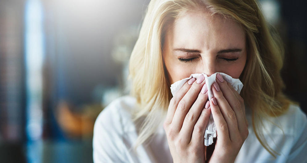 A person sneezing into a tissue, possibly indicating cold or allergy symptoms