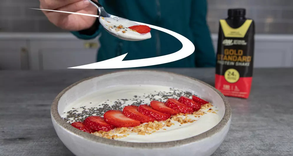 Bowl of yogurt topped with strawberries and chia seeds, with Optimum Nutrition Gold Standard protein shake in the background