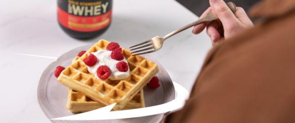 Optimum Nutrition Gold Standard 100% Whey Protein container next to a plate of waffles topped with yogurt and raspberries