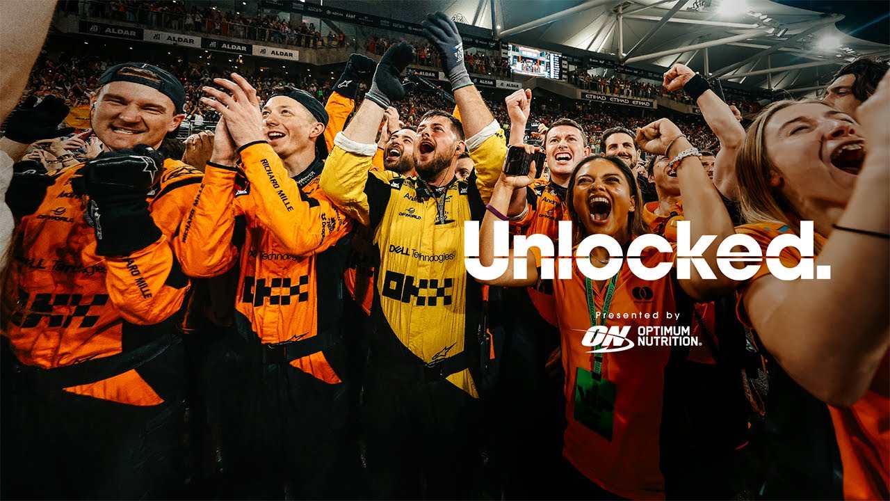 A group of people in orange and black uniforms celebrating at an event. Optimum Nutrition logo is visible