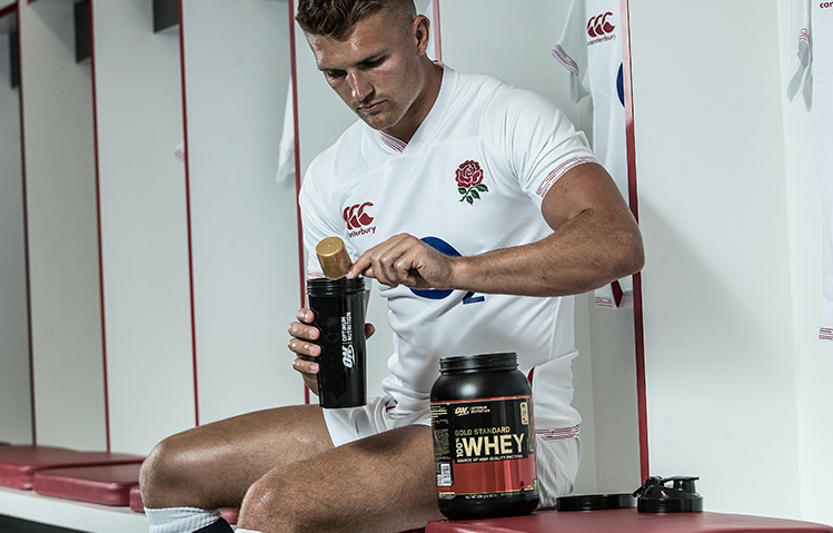rugby player in locker room having protein powder after a match