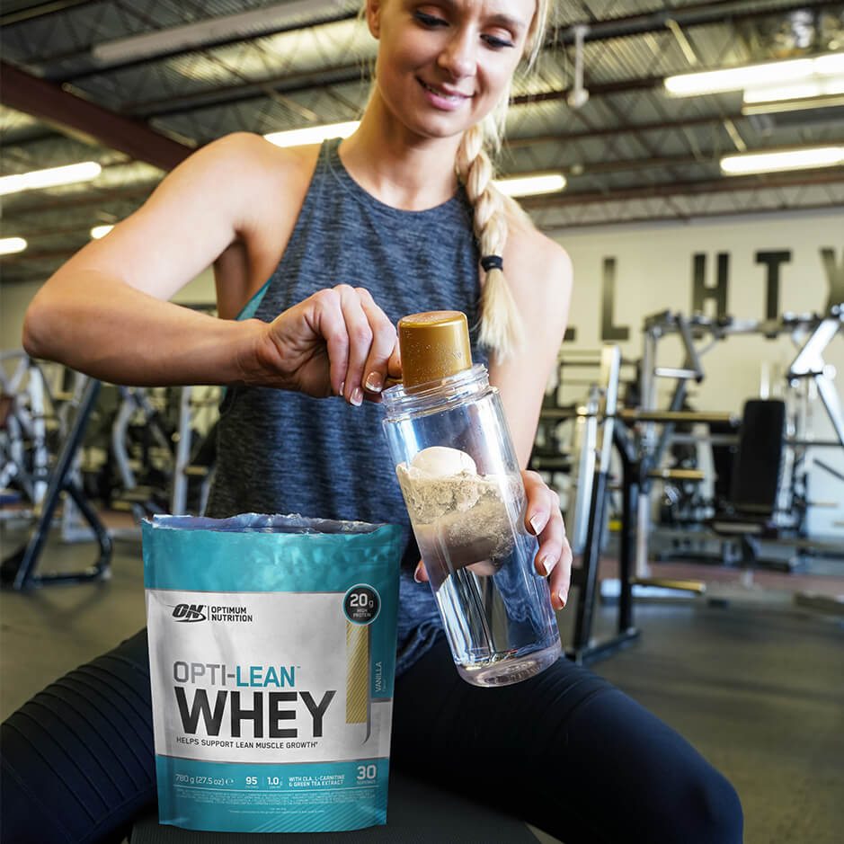 a woman putting a scoop of opti-lean whey in shaker in gym