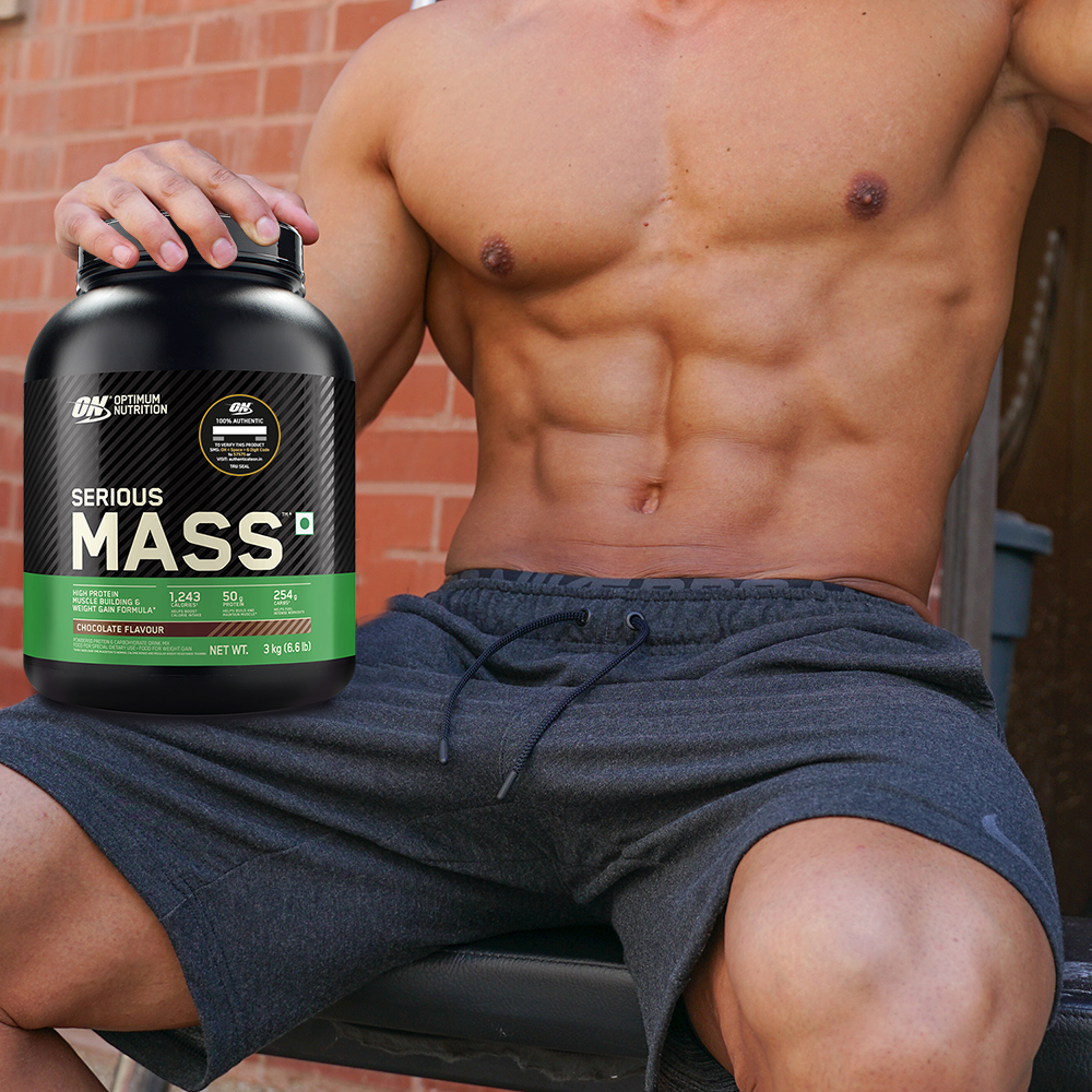 a man with his top off holding a tub of serious mass for vegatarians