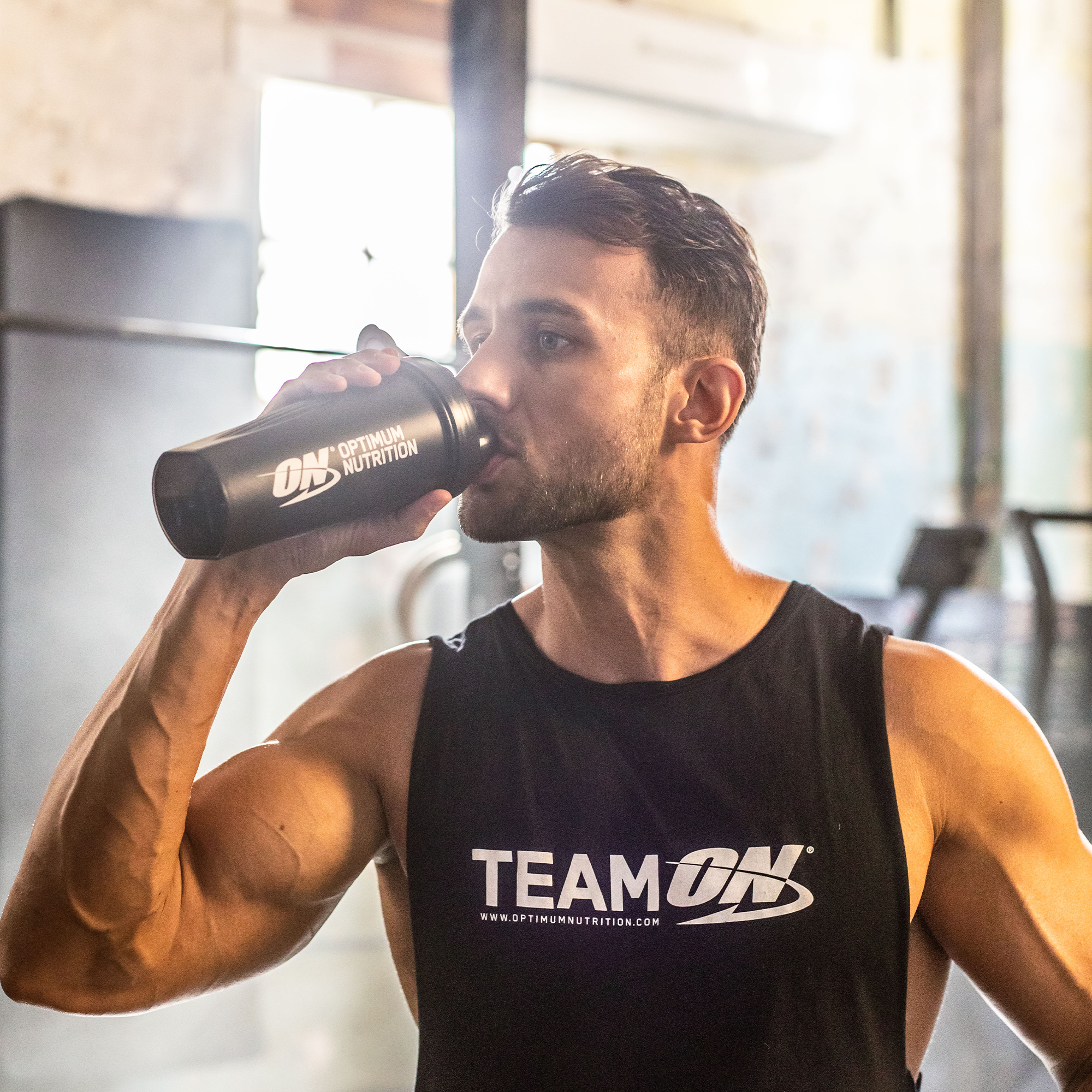 man in a gym drinking from an optimum nutrition shaker